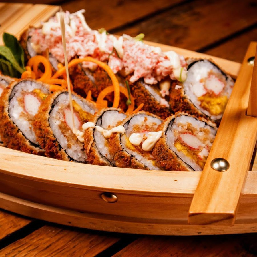 Barco lleno de rollos tempura con salsa cremosa y vegetales